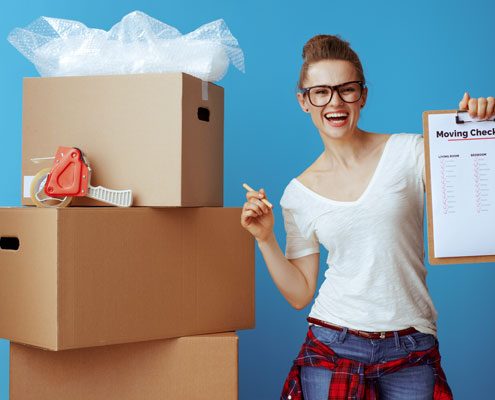 Moving house checklist. Woman standing infront of packing boxes while holding a checklist.