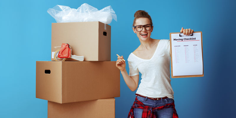 Moving house checklist. Woman standing infront of packing boxes while holding a checklist.