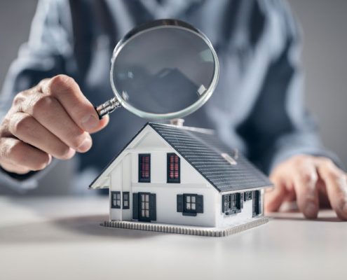 Your property inspection check list. Man holding a magnifying glass over a model house inspecting the detail.