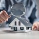 Your property inspection check list. Man holding a magnifying glass over a model house inspecting the detail.